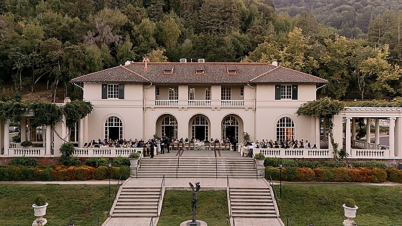 Outdoor wedding reception with long banquet tables and white linens under string lights on a villa terrace with arched windows and vines