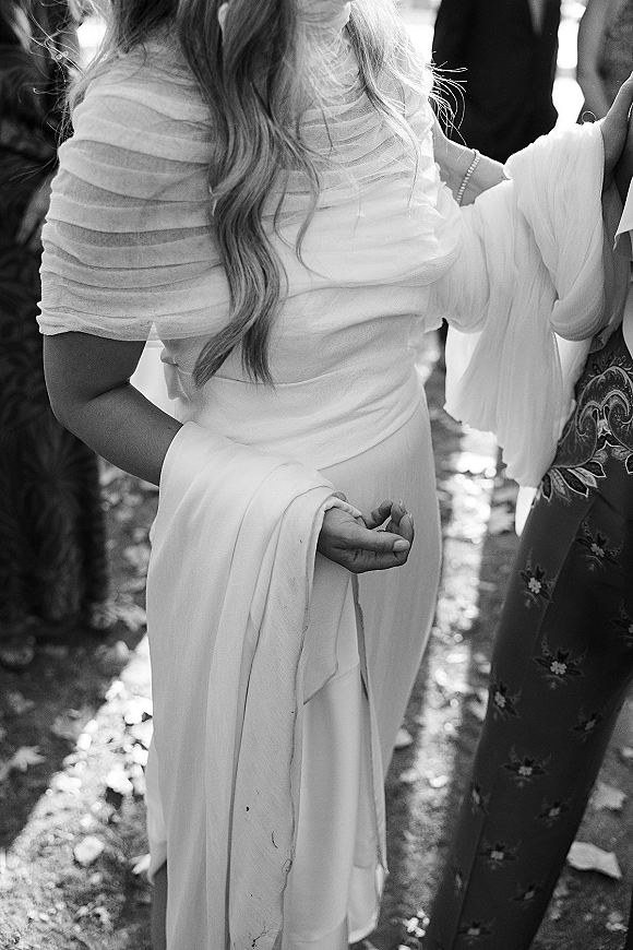 Wedding guest dress in white with an off-the-shoulder ruched bodice and long sleeves, worn on an outdoor walkway in dappled sunlight