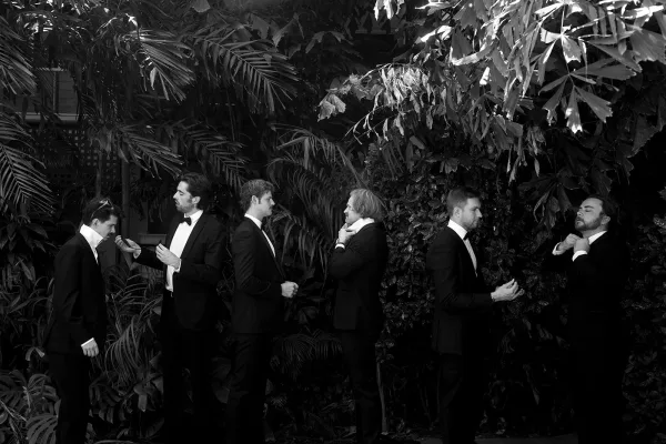 Groomsmen portrait in tuxedos and bow ties with boutonnieres, posed together against a lush tropical greenery wall backdrop