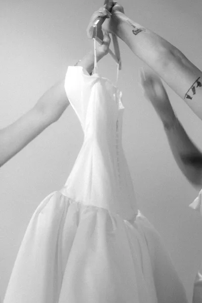 Wedding dress on a hanger with button-back detail against a plain wall, minimalist bridal gown displayed for getting-ready photos