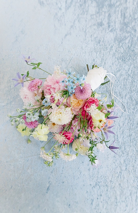 Bridal bouquet with pastel bridal bouquet blooms and greenery, ribbon-wrapped handle on a light blue textured backdrop flat lay