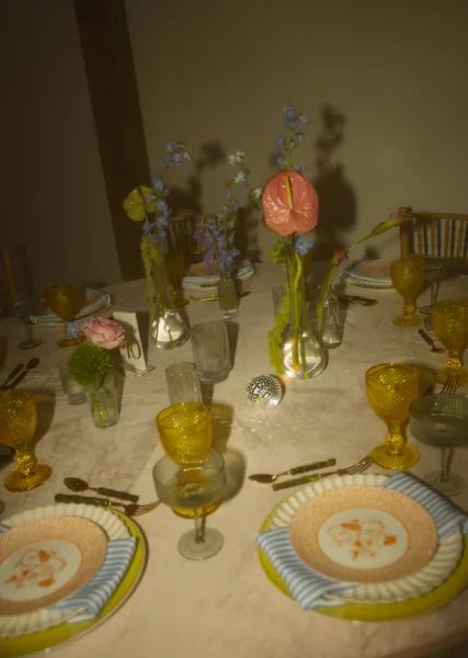 Reception tablescape wedding table setting with bud vase florals, amber goblets, gold flatware, striped napkins, and a small disco ball indoors