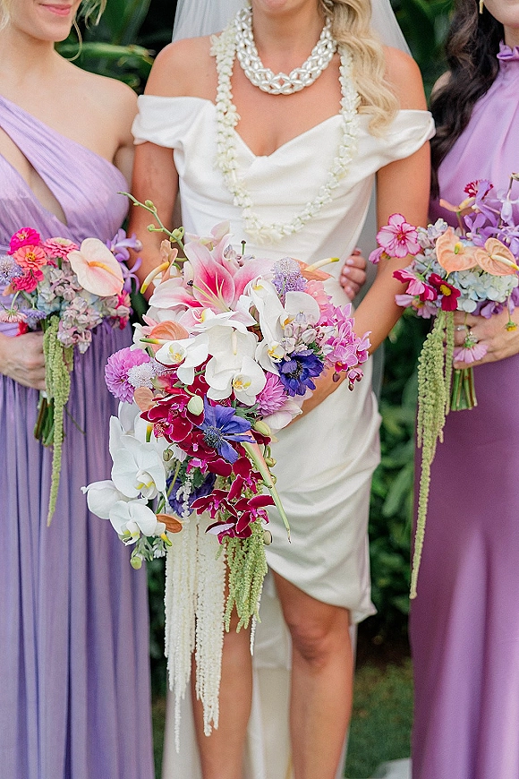 Bridesmaid bouquet photo showing a tropical wedding bouquet with orchids, lilies, anemones, and cascading amaranthus against garden greenery