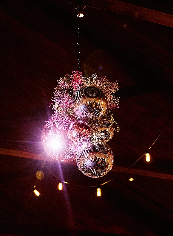 Disco ball decor with hanging disco ball centerpiece, baby's breath and string lights suspended from wooden beams under a dark ceiling