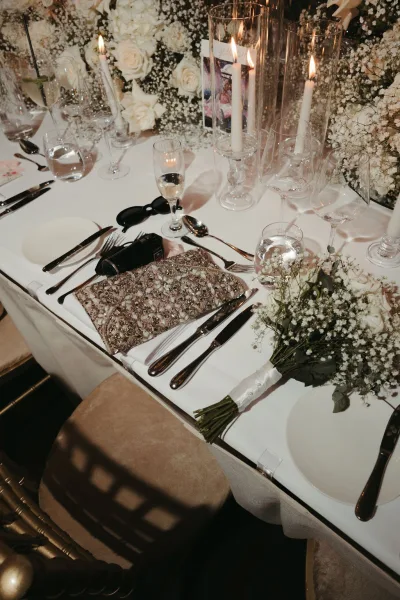 Wedding table decor set for a candlelit reception table, with taper candles casting a warm glow across the minimalist white tablescape.