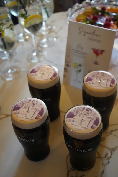 Wedding signature drink display with personalized beer pints crowned by edible photo toppers on a polished marble tabletop.