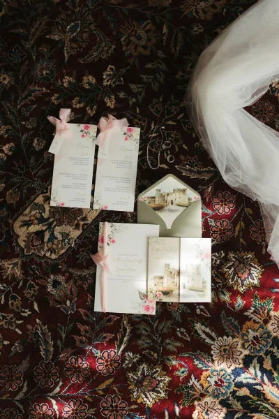 Wedding invitation suite with floral wedding invitations and wedding rings, artfully styled as a flat lay on a patterned rug.