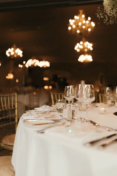 Reception tablescape for a wedding table setting with votive candles, beneath chandeliers in an elegant ballroom of round tables