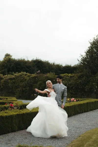 Couple portrait with the bride twirling dress as the groom spins her along a rose garden walkway, her tulle bridal gown catching the light.