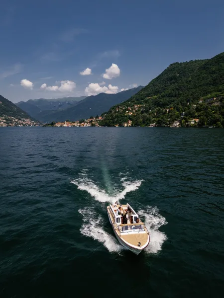 Wedding boat ride with newlyweds on boat in a wood speedboat, bride in her dress and groom in suit on a mountain lake near a hillside village