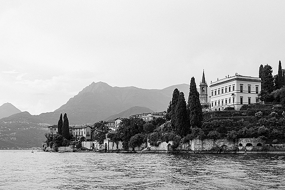 Wedding venue landscape overlooking a lakeside wedding venue with a historic villa, bell tower, cypress trees, and mountains beyond the shore