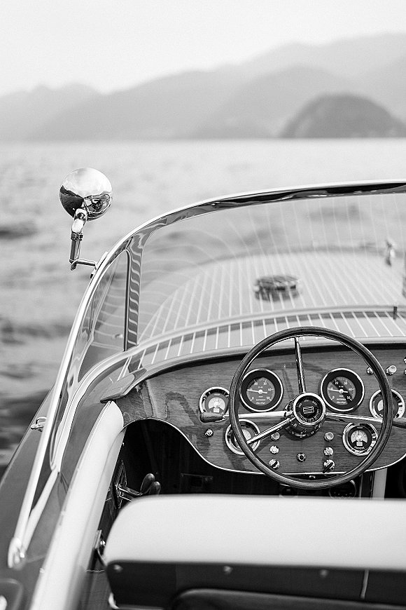 Vintage boat detail of a classic wooden speedboat cockpit with steering wheel, dashboard gauges and chrome mirror on a mountain lake