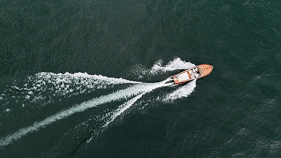 Wedding getaway boat with white upholstery and a trailing wake, captured from above as it speeds across open water