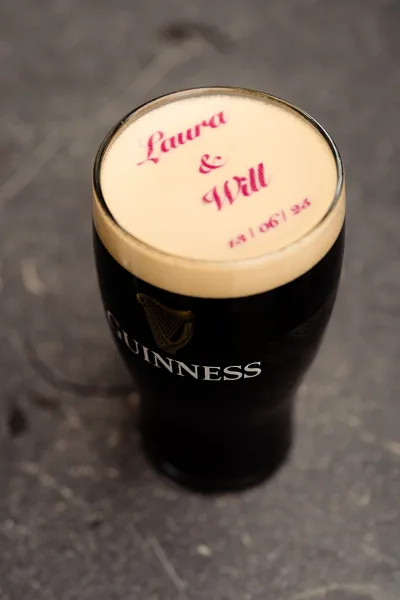 Wedding drink detail featuring a personalized beer in a pint glass with a printed foam topper on a stone bar top