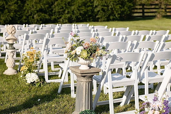 Ceremony seating with outdoor wedding ceremony chairs in neat rows, white folding chairs beside a floral urn on a grassy lawn near hedges