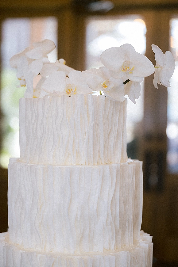 Wedding cake with a white orchid cake topper, tiered textured buttercream frosting, lit by window light in an indoor reception space