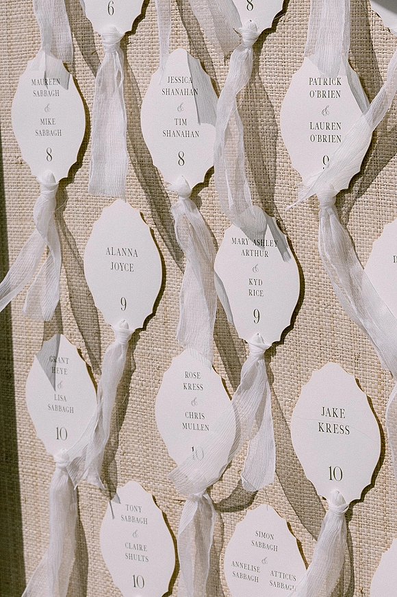 Wedding escort cards with wedding seating cards on deckle edge tags tied with white ribbon and table numbers against a textured linen backdrop