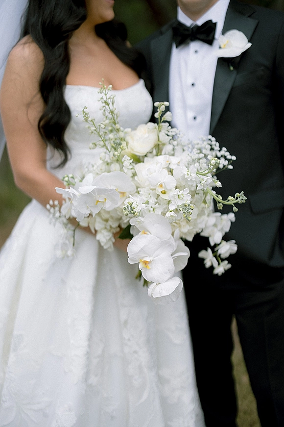 Couple portrait of bride and groom portrait with strapless gown and black tuxedo, bride holding white orchid and baby's breath bouquet outdoors
