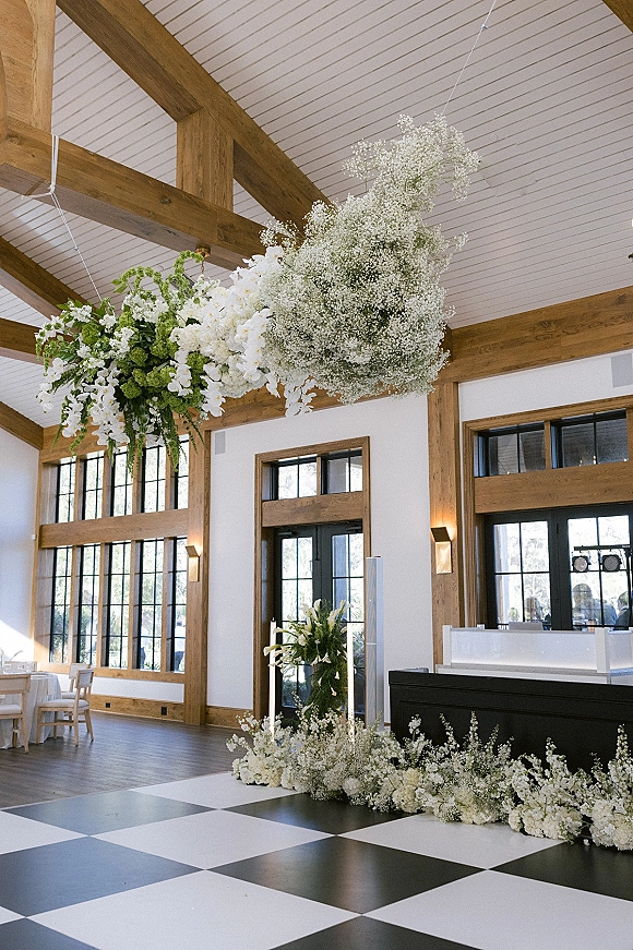 Wedding reception decor with hanging floral installation of baby’s breath over a black-and-white checkered dance floor in a bright hall