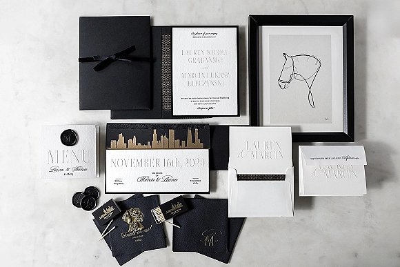 Invitation suite of black and white wedding invitations with gold foil, wax seal, ribbon, and RSVP cards on a white marble surface