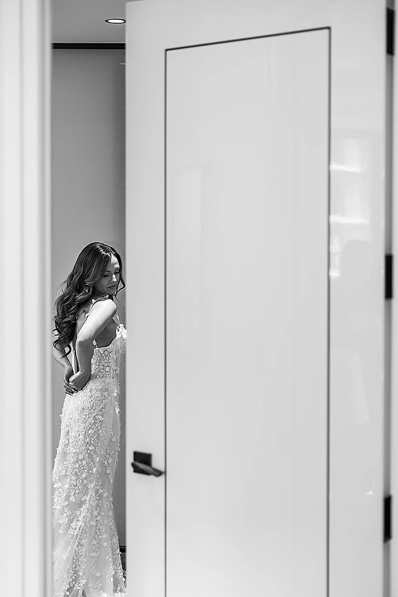 Bridal portrait of a bride in a doorway showing bridal dress back detail with a lace wedding dress, low-back gown and long curls indoors