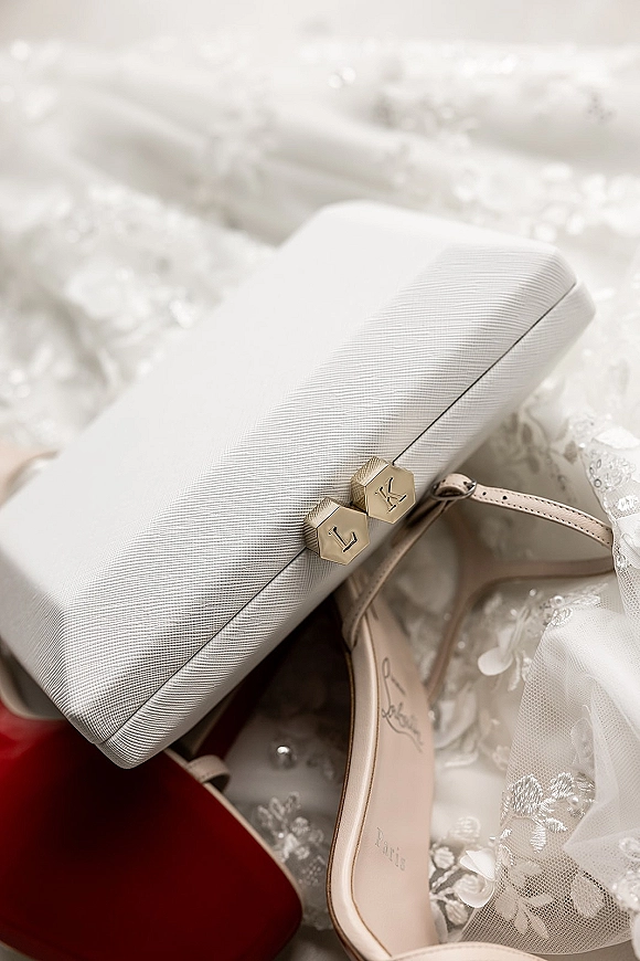 Bridal accessories flat lay with a wedding clutch purse, strappy heels and white clutch with gold clasp on lace tulle fabric background