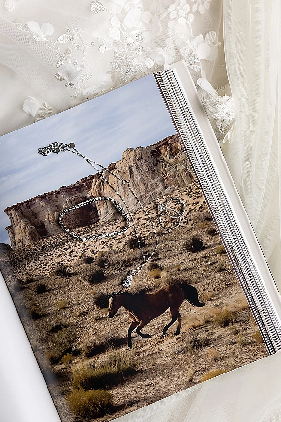Wedding rings in a wedding ring flat lay beside a diamond engagement ring on a printed photo page with desert cliffs in the background