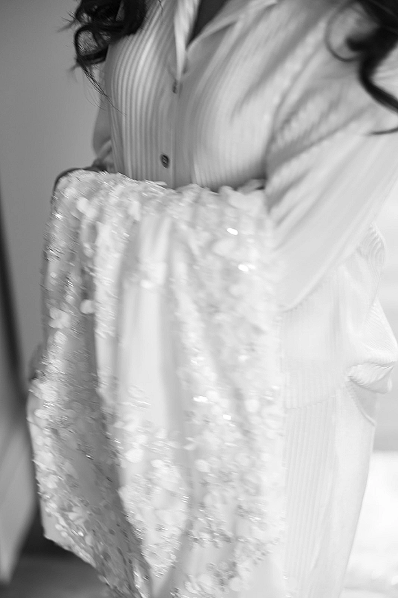 Wedding dress close-up showing lace appliqué with beading and sequins, framed beside a button-front pajama top against an indoor wall