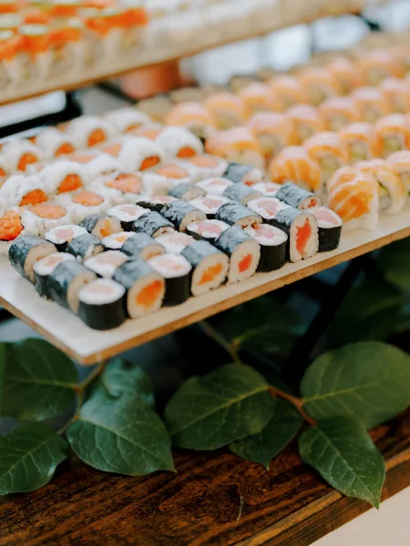 Wedding sushi platter arranged on wooden serving trays with assorted rolls and nigiri, finished with a greenery garland on a wood table