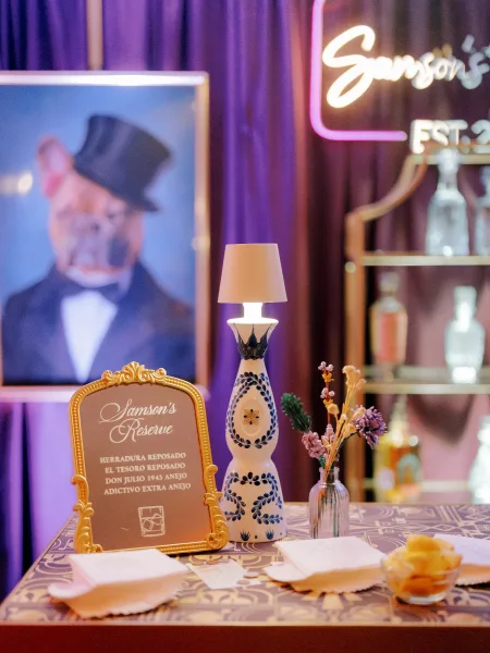 Wedding bar decor with a wedding tequila bar display, custom bar sign, framed portrait, and neon accent against draped curtains