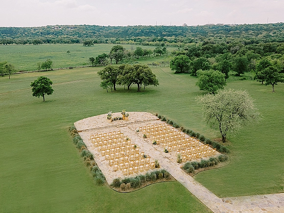 Ceremony setup with outdoor ceremony seating, wood crossback chairs lining a stone aisle to altar flowers on a patio, hills beyond