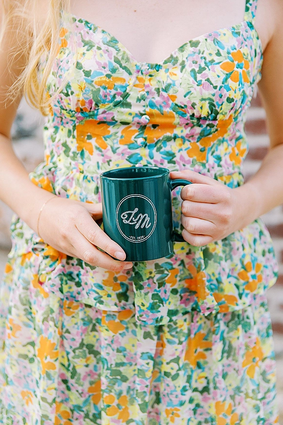 Custom monogram mug held in hand, a bridesmaid proposal mug beside a colorful floral dress on brick steps, teal ceramic finish