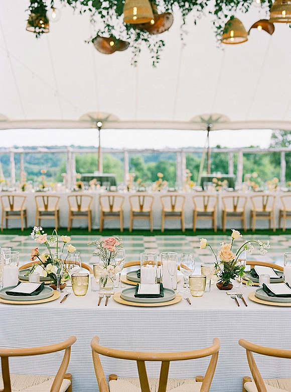 Reception tablescape with sage green plates, gold chargers and amber glassware, accented by white taper candles under a white tent canopy