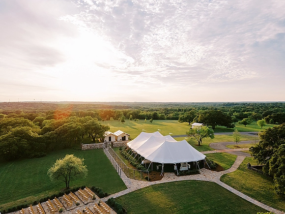 Outdoor wedding tent with sailcloth wedding tent canopy, ceremony chairs on a stone patio and walkways, set on a lawn at sunset