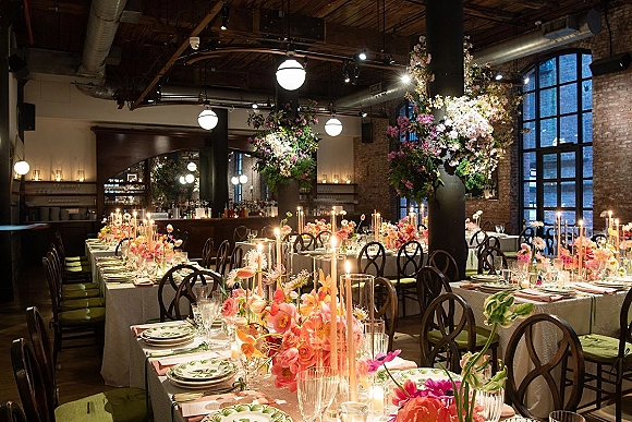 Reception tablescape with colorful wedding tablescape florals, tall taper candles, and place settings on long tables in an industrial brick loft