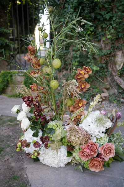 Wedding floral arrangement with orchids, hydrangeas, and roses spilling over greenery on a stone path by an ivy wall and garden gate