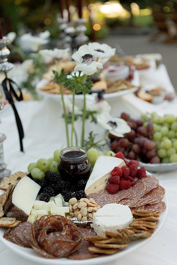 Wedding charcuterie board cheese and charcuterie platter with brie, salami, berries, grapes, nuts and jam on a garden table with candlesticks