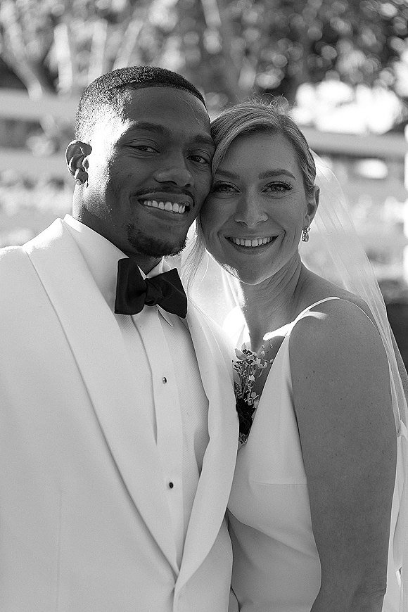 Couple portrait, black and white wedding portrait of bride and groom smiling cheek to cheek, veil and tuxedo, soft trees bokeh behind