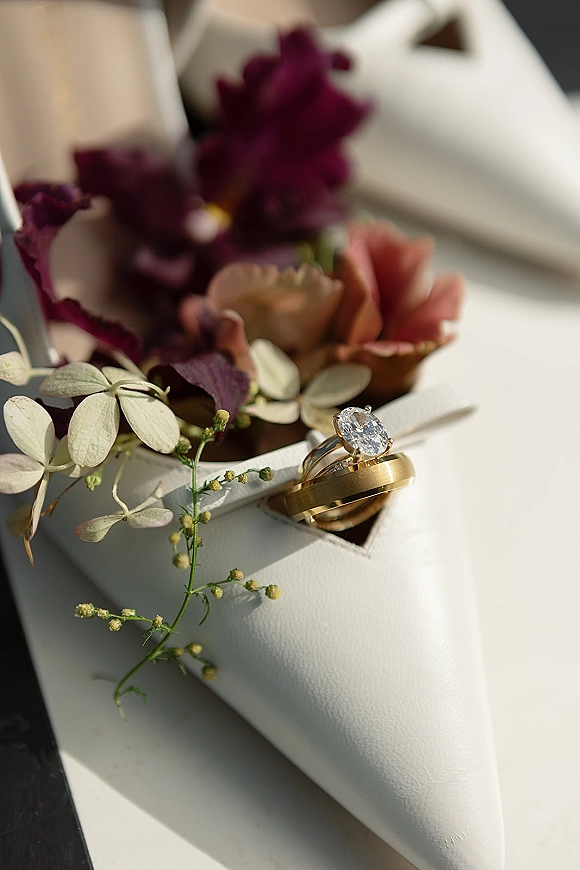 Wedding rings and engagement ring close up on a white ring box with dried florals and ribbon on a soft neutral tabletop background