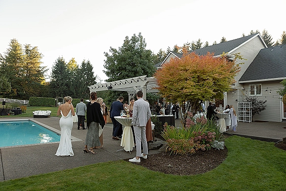 Wedding cocktail hour with outdoor cocktail hour tables, linen high tops and drinks under string lights by a poolside patio and pergola