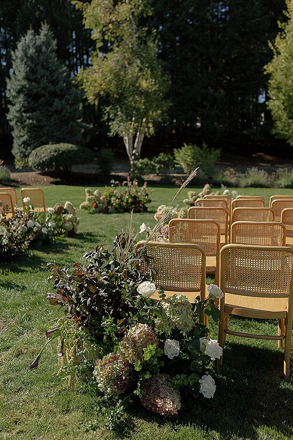 Ceremony seating with outdoor ceremony chairs in rattan rows, lined with hydrangeas, roses, calla lilies and greenery on a garden lawn