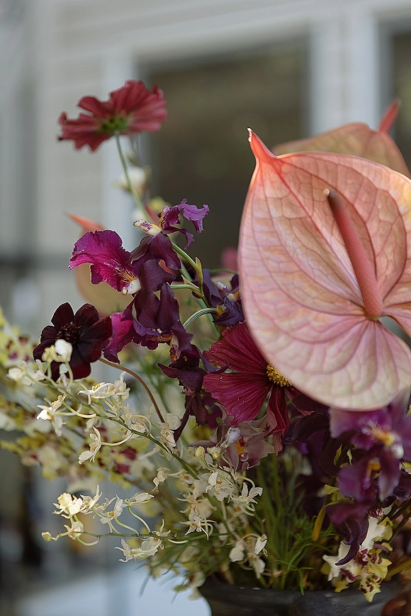 Wedding flowers with anthurium and orchids in a lush floral arrangement, styled by a window against a neutral wall backdrop