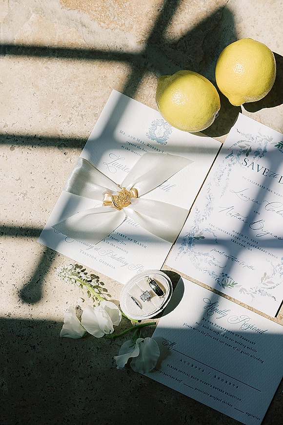 Invitation suite wedding invitation flat lay with save the date and RSVP cards, wax seal, rings, ribbon, lemons on stone in window light