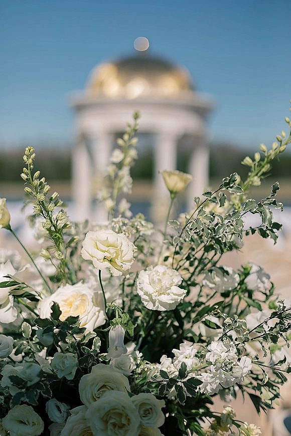 Ceremony florals with wedding ceremony flowers in white roses and greenery at an outdoor gazebo pavilion overlooking sky and water