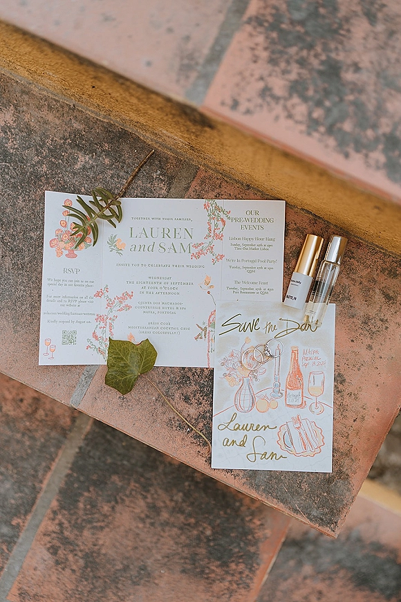 Invitation suite wedding invitation flat lay with illustrated cards, save the date, RSVP, rings and perfume on terracotta tile steps with leaf sprigs