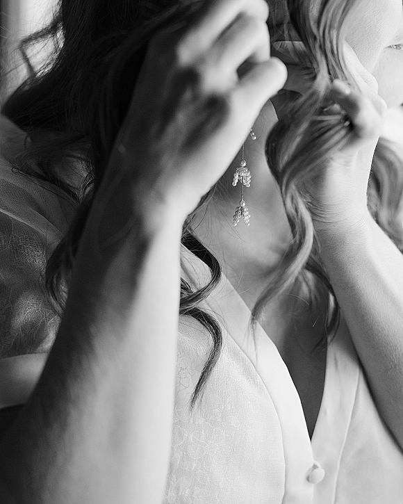 Bridal earrings, pearl drop earrings dangling from the bride’s ear as she gets ready in a robe by soft window light in an interior room