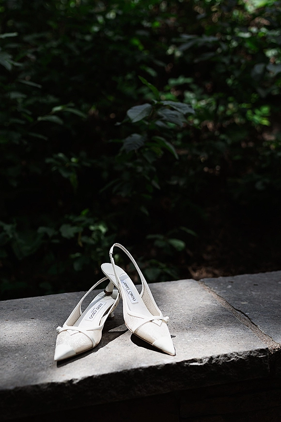Wedding shoes in ivory bridal shoes style, slingback pointed-toe heels resting on a stone ledge with soft greenery behind