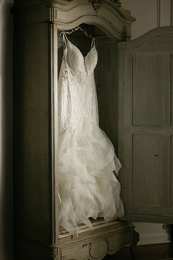 Wedding dress with lace wedding dress bodice and spaghetti straps hanging on a hanger in a vintage armoire with open wardrobe door