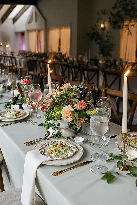 Reception tablescape with wedding head table decor, brass taper candles and lush florals on a long banquet table in an elegant hall