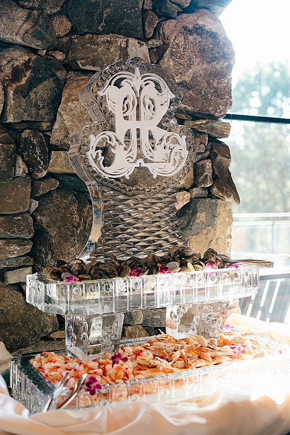 Ice sculpture display with wedding ice sculpture monogram, holding shrimp and clams on buffet trays with orchid accents by a stone wall